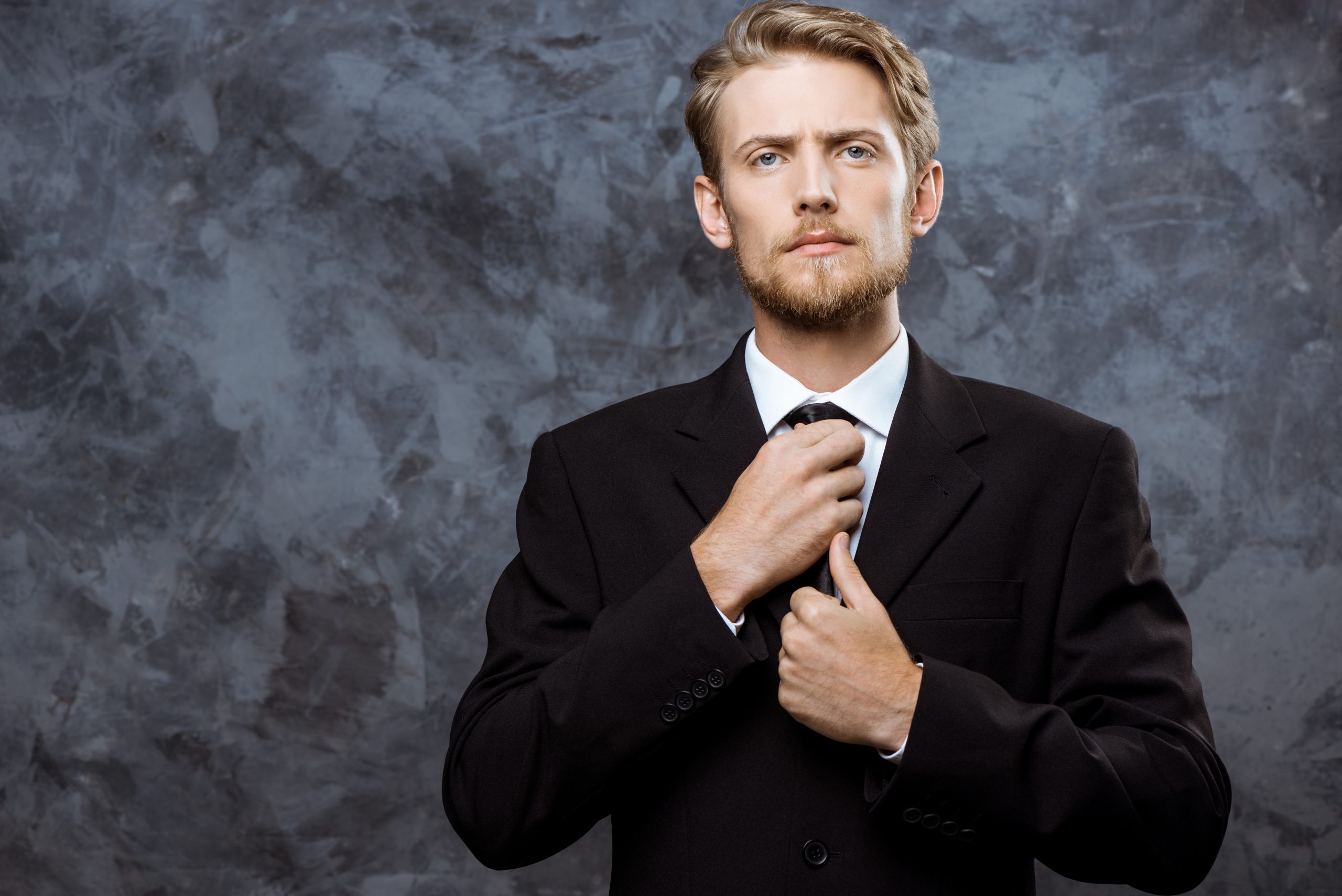 Young successful businessman correcting tie over grey background.